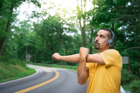 Young fitness man runner with earphones stretching before run in road in nature. Healthy lifestyle and sport conceptsの写真素材