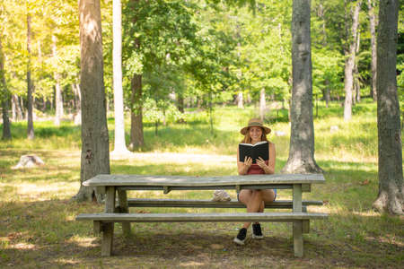 Happy woman smiling and reading book in nature. Hobby and lifestyle concept. Faith, spirituality and religion. Charming girl student.の写真素材