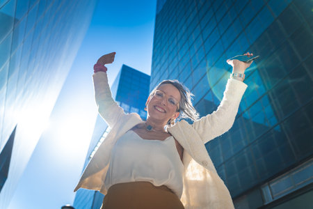 Happy businesswoman celebrating good news in front of business buildings.の写真素材