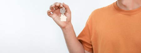 Banner of young man with the new home keys. Keychain in the shape of a wooden house on white...