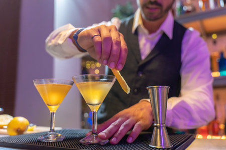 Handsome barman making elegant cocktail in night club on bar counter with lights at nightclub party.