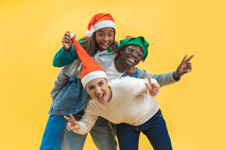 Happy three multiracial friends celebrating excited Christmas in yellow studio background.の写真素材
