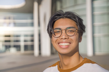 Handsome asian young man happy smiling outdoors in the student campus during a sunny day.の写真素材