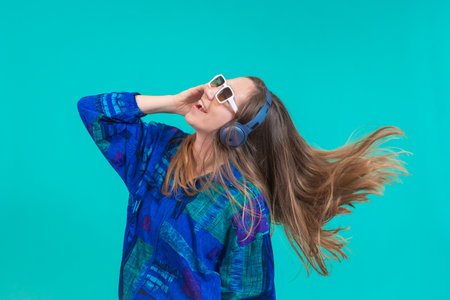 Energy girl with blue headphones listening to music dancing isolated on blue background in studio.