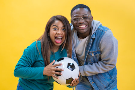 Excited ethnic diversity couple enjoying soccer together isolated on yellow background happy.の写真素材