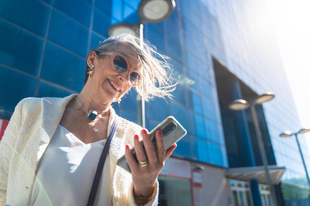 Attractive middle aged business woman looking at her smart phone in the street.の写真素材