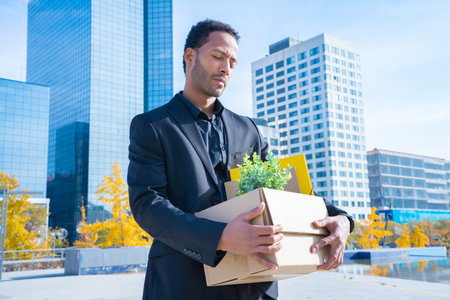 Businessman with cardboard box with office supplies standing outside office building. Fired conceptの写真素材
