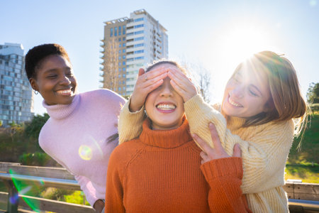 Female friends covering each other eyes for a surprise. Girls having fun together laughing.の写真素材