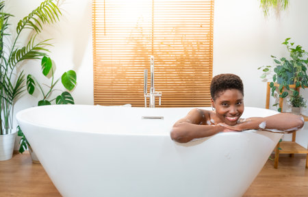 Luxury bath portrait of an attractive African woman relaxing in bathtub at cozy home bathroom.