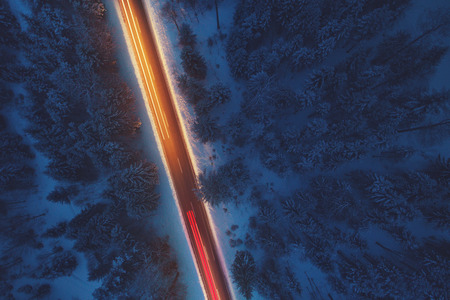 Top down view to road in the snowy wood. Romantic night aerial photo of cars traveling on the mountain road.の写真素材