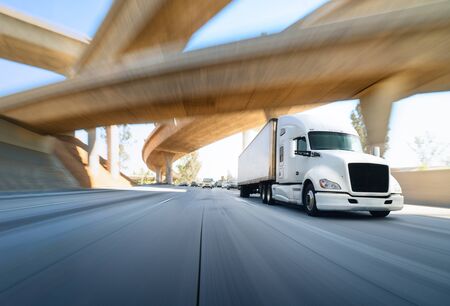 American style truck on freeway pulling load. Transportation theme. Road cars theme. Truckers heaven. Trailer passing the bridgeの写真素材