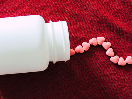Love Heart tablets in a white bottle on red cloth background. Valentines day.の写真素材