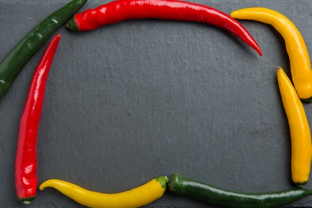 three colorsr chili peppers on a dark slate stone slabの写真素材