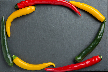 three colorsr chili peppers on a dark slate stone slabの写真素材