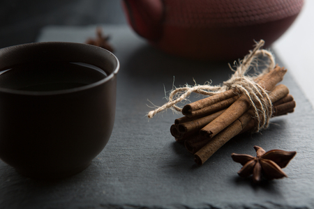 Iron teapot and traditional ceramic cup of tea with bunch of cinnamon sticks and star anise. Asian style.の写真素材