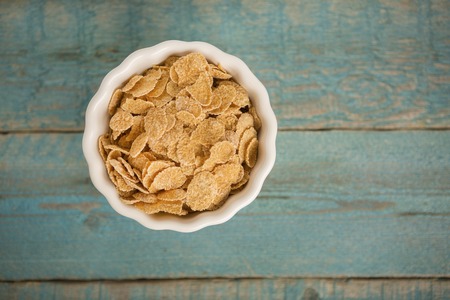 Crunchy cornflakes cereals in white bowl on old wooden table at morning breakfast