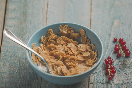 Organic corn or oat or cereal or barley flakes in blue porcelain bowl with red currant on old wooden tableの写真素材