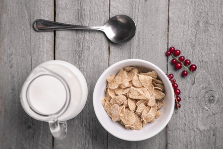 Organic corn or oat or cereal or barley flakes in blue porcelain bowl with red currant and jug of...