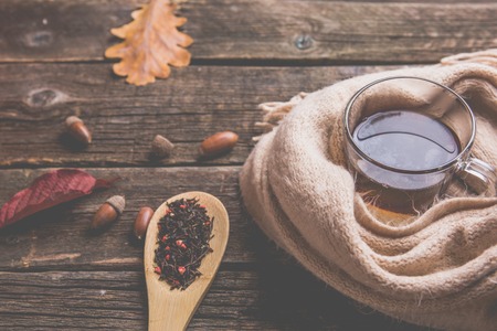 Autumn composition, fall leaves,acorns , glass cup of tea and a warm scarf on old wooden table background.の写真素材