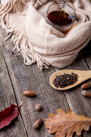 Autumn composition, fall leaves,acorns , glass cup of tea and a warm scarf on old wooden table background.の写真素材
