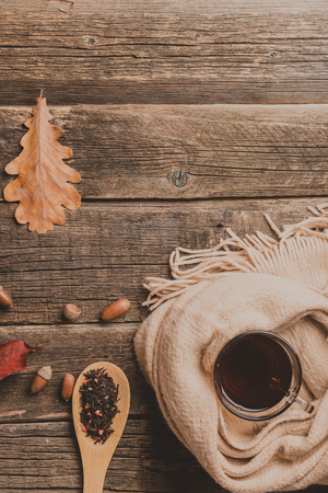 Autumn composition, fall leaves,acorns , glass cup of tea and a warm scarf on old wooden table background.の写真素材