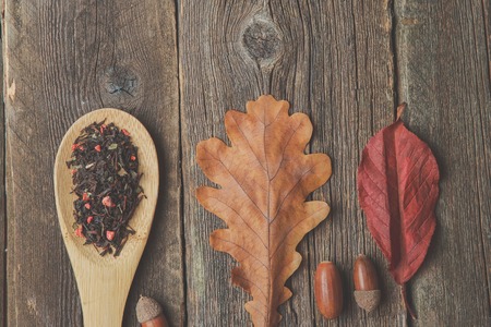 Cup of tea with autumn leaves, acorns and spoonful dry herbal tea on wooden table. Toned photo
