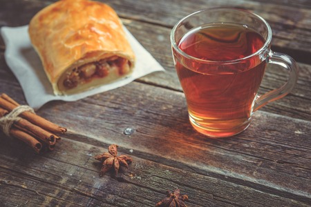Homemade apple strudel with fresh apples,raisins and cup of hot tea drink on wooden background....