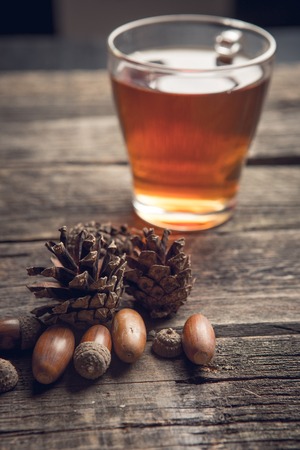 Autumn background concept on a wooden table with a glass cup of tea, Pine cones and acornsの写真素材