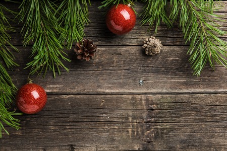evergreen fir twigs with shiny red baubles and pine cones on old wooden backgroundの写真素材