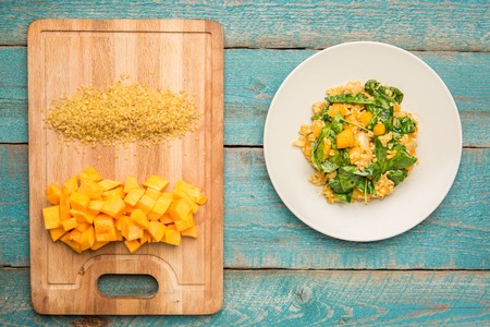 Plate with bulgur and pumpkin with spinach near cutting board with ingredients on old blue backgroundの写真素材