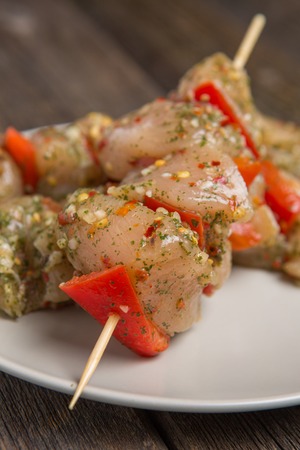 skewers of raw chicken meat and vegetables on light plate on dark wooden backgroundの写真素材