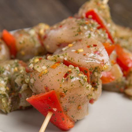 skewers of raw chicken meat and vegetables on light plate on dark wooden backgroundの写真素材