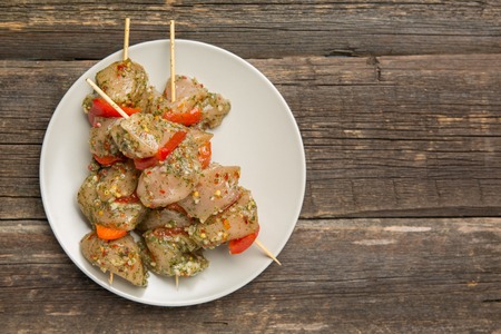 skewers of raw chicken meat and vegetables on light plate on dark wooden backgroundの写真素材