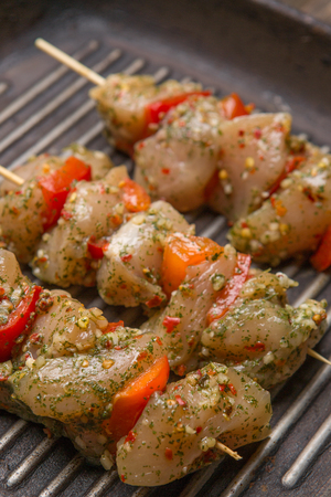 Raw chicken skewers with vegetables and spices on black cast iron grill panの写真素材