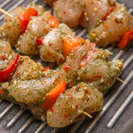 Raw chicken skewers with vegetables and spices on black cast iron grill panの写真素材