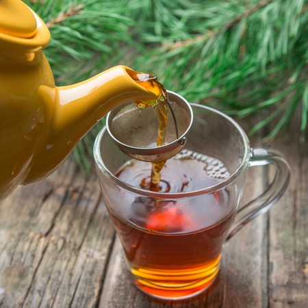 Process of pouring tea from the kettle of yellow color into the glass cup on wooden texture backgroundの写真素材