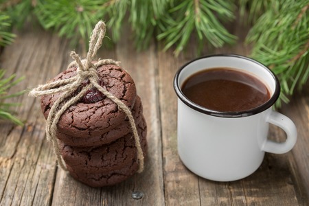 Winter decoration with Homemade Christmas chocolate cookies with cranberry tied with twine and enamel mug full of coffee on wooden table. Selective focusの写真素材