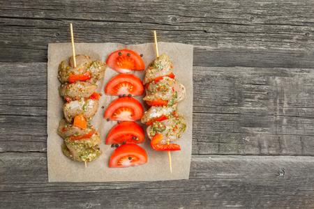 Chicken kebab - raw meat on skewers on paper with tomatos on aged wooden background. Flat lay, copy space. Selective focus.の写真素材