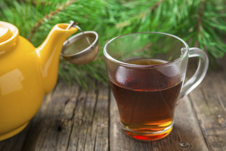 Yellow teapot with glass cup of tea and fir tree branches on old wooden background. Christmas and New Year treat.の写真素材