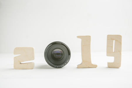 Wooden number 2019 on white wooden background with camera photo lens instead of 0