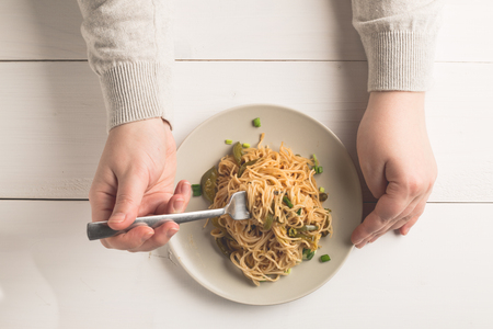 Spaghetti on white plate. Fusion cuisine food style. A female hand is trying to use fork to eat.の写真素材