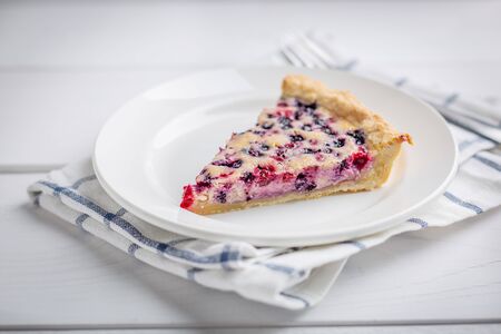 Slice of Blueberry and red currant Pie on white rustic wooden table