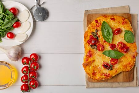 Homemade pizza with tomatoes, garlic ,mozzarella and basil. Top view on white tableの写真素材