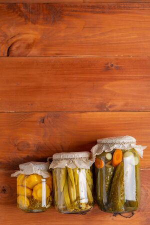 Salting various vegetables in glass jars for long-term storage. Preserves vegetables in glass jars on brown rustic wooden background. Top view.の写真素材