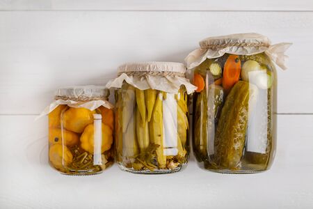 Salting various vegetables in glass jars for long-term storage. Preserves vegetables in glass jars on white wooden background. Top view.の写真素材