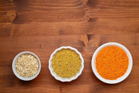 Healthy food, dieting, nutrition concept, vegan protein source. Raw of legumes , red lentils, bulgur, oak flakes in white bowls. Top view with copy spaceの写真素材