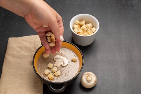 Woman adding croutons to delicious mushroom cream soup at black tableの写真素材