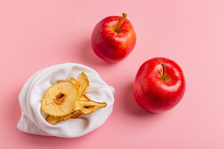 Homemade sun-dried organic crispy apple chips in cloth bag, on pink background with fresh apple....