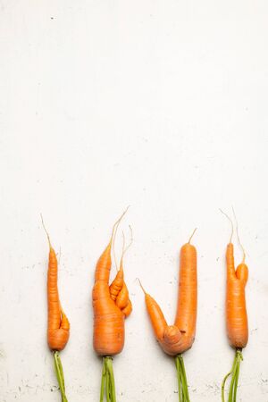 Ugly carrots on a white cracked surface. Ugly food concept, top view.の写真素材