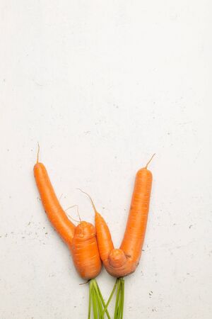 Funny ugly carrots on threadbare white surface top view with copy space.の写真素材